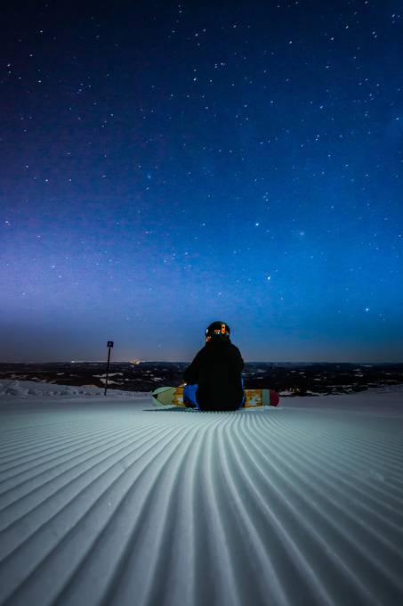 座って星空を見つめるスノーボーダーの写真