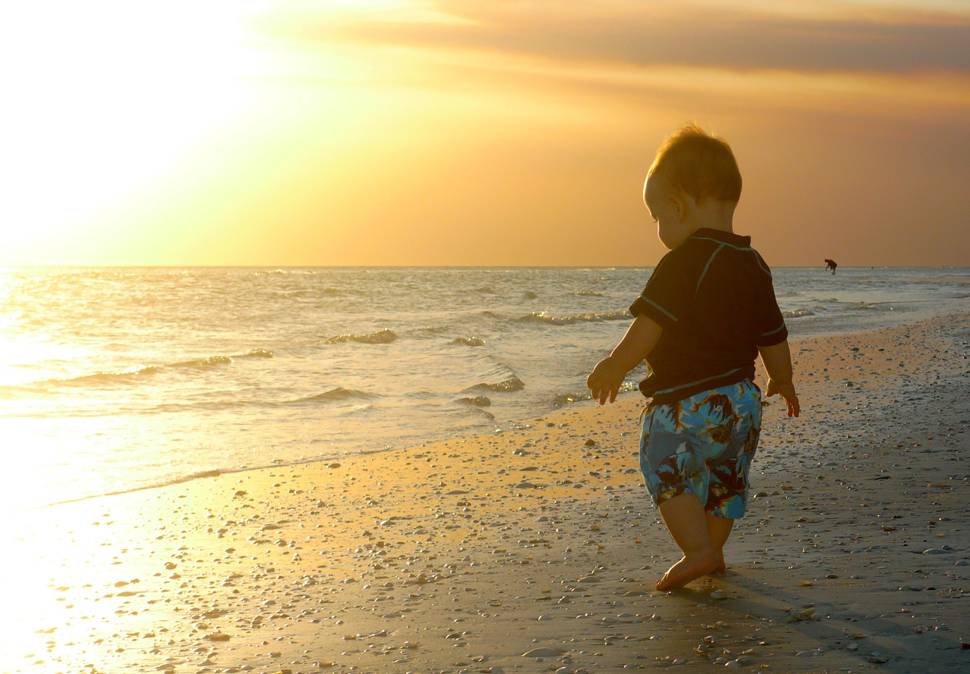 夕焼けに染まった海辺を歩く男の子の写真