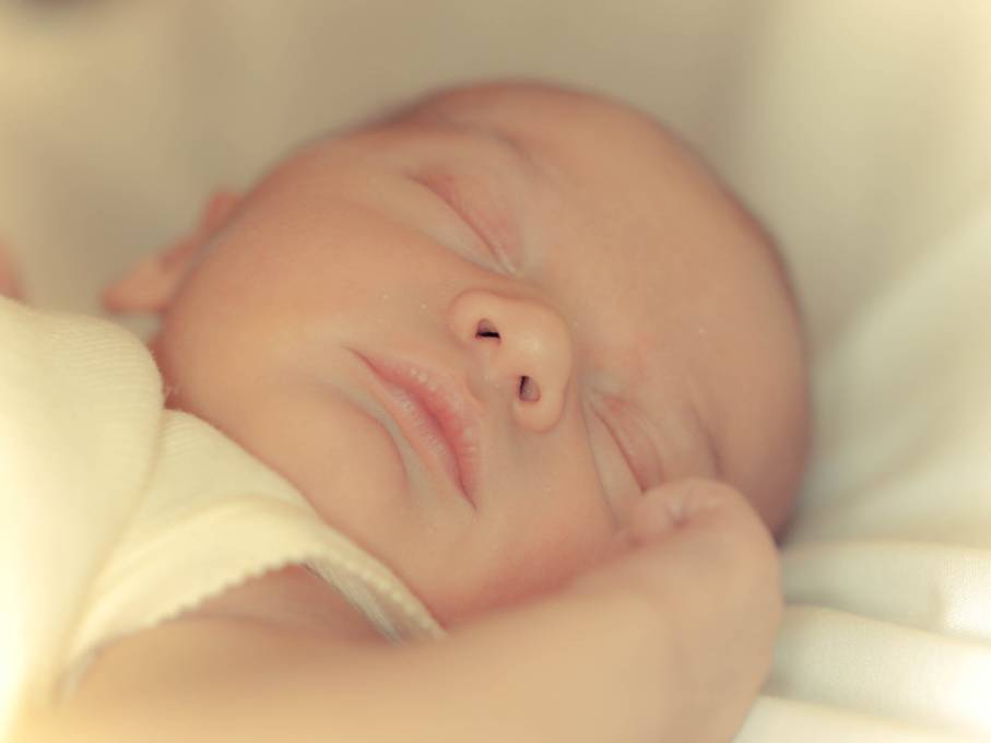 柔らかいシーツの上で眠る新生児の写真