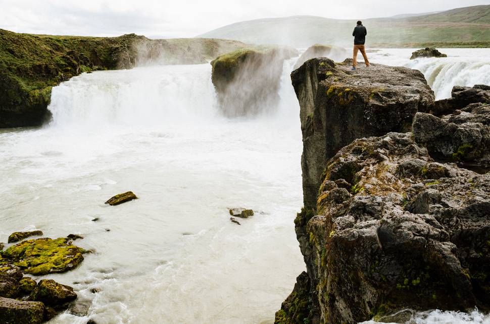 滝の降り注ぐ崖の上に佇む男性の絶景な写真