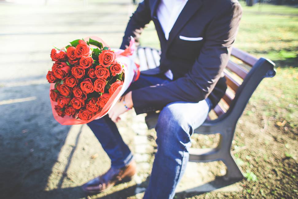 バラの花束を持ってベンチに座る男性の写真